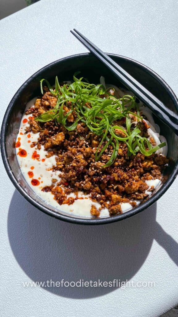 Bowl of creamy mapo tofu udon noodles topped with spicy tofu crumble, chili oil, and green onions