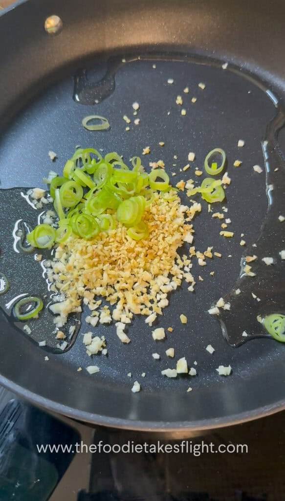 Garlic, ginger, and green onions sautéing in oil in a pan