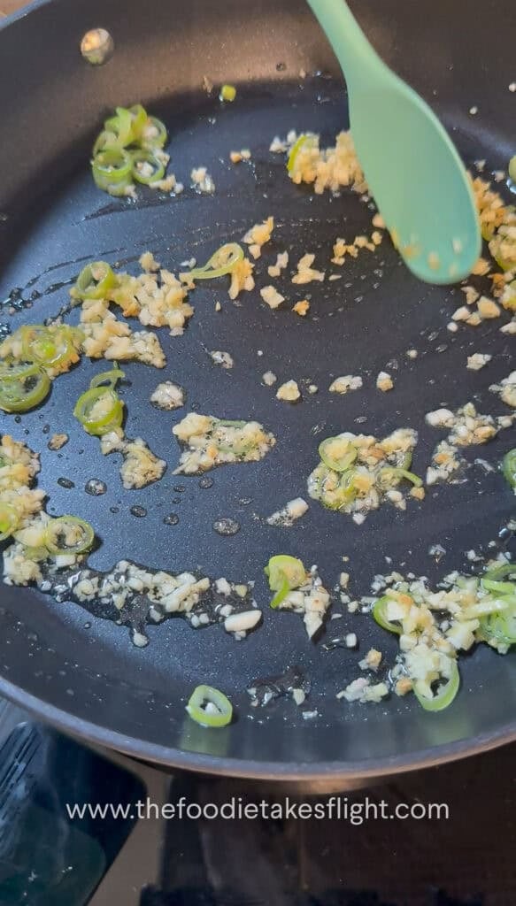 Garlic, ginger, and green onions sautéing in oil in a pan