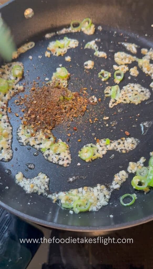 Garlic, ginger, and green onions sautéing in oil in a pan