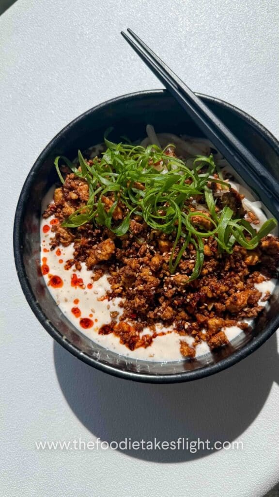 Bowl of creamy mapo tofu udon noodles topped with spicy tofu crumble, chili oil, and green onions