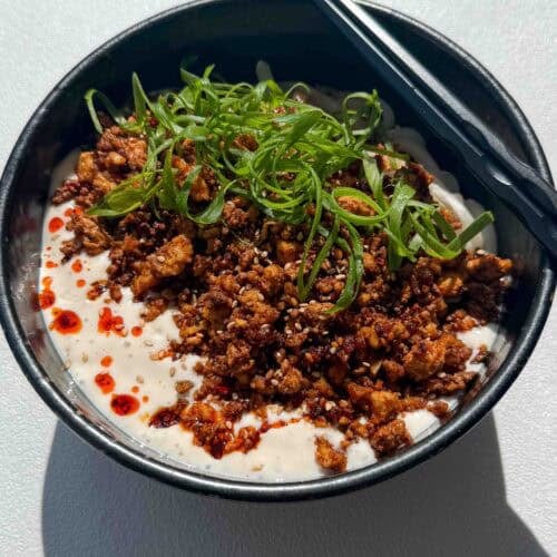 Bowl of creamy mapo tofu udon noodles topped with spicy tofu crumble, chili oil, and green onions