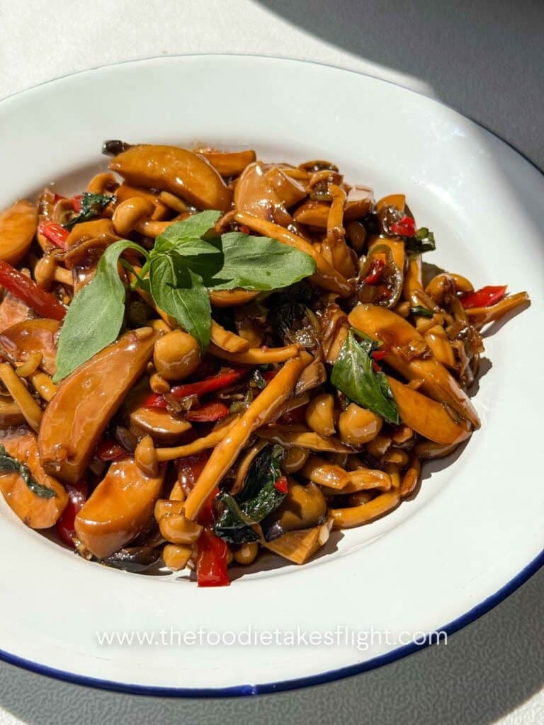 Close-up of Thai-style mushroom kra pao with glossy mushrooms, peppers, and basil leaves 