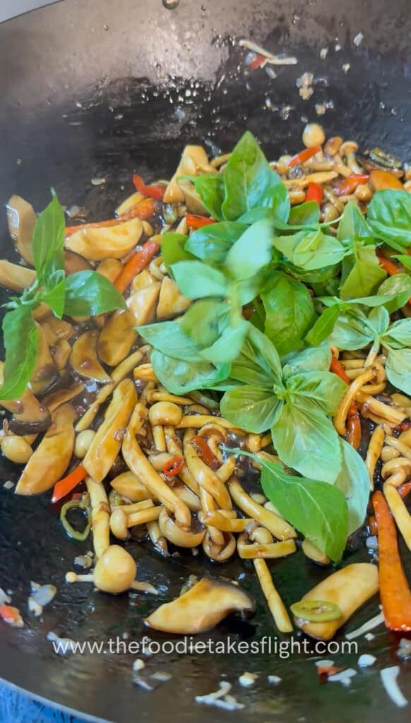 Fresh holy basil or Thai basil leaves being folded into the mushroom stir-fry