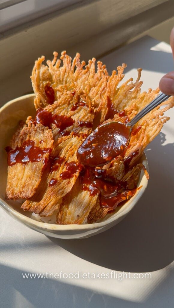 Crispy pan-fried enoki mushrooms served over rice with gochujang sauce, scallions, and sesame seeds