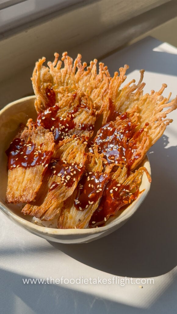 Crispy pan-fried enoki mushrooms served over rice with gochujang sauce, scallions, and sesame seeds