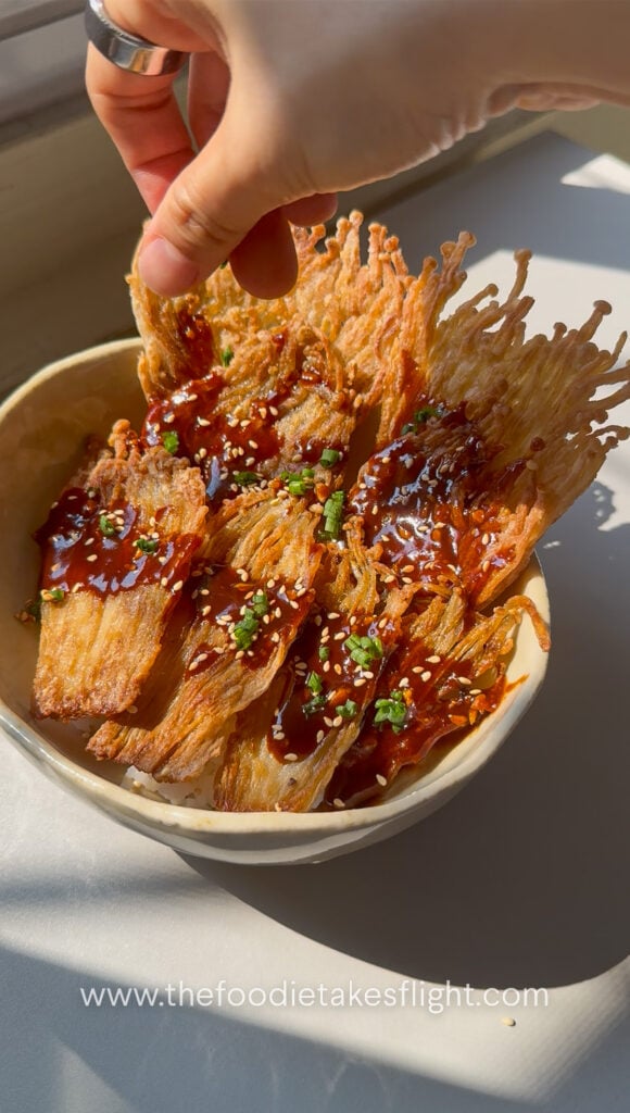 Crispy pan-fried enoki mushrooms served over rice with gochujang sauce, scallions, and sesame seeds