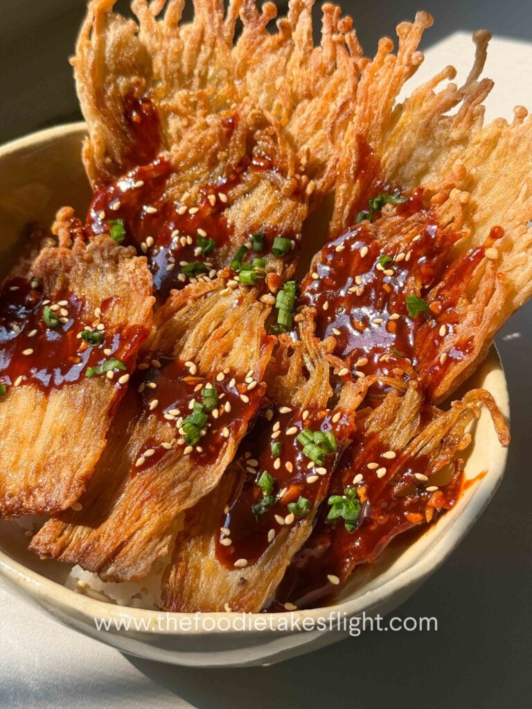 Crispy pan-fried enoki mushrooms served over rice with gochujang sauce, scallions, and sesame seeds
