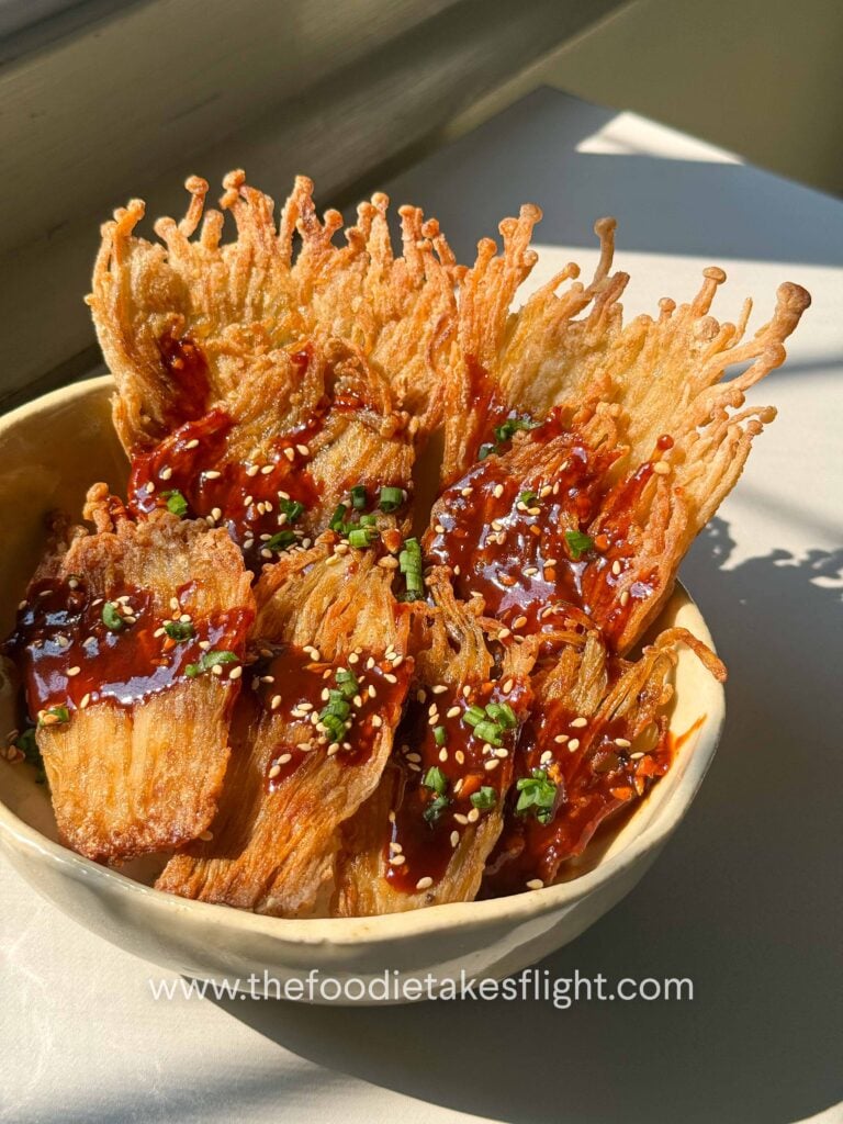 Crispy pan-fried enoki mushrooms served over rice with gochujang sauce, scallions, and sesame seeds
