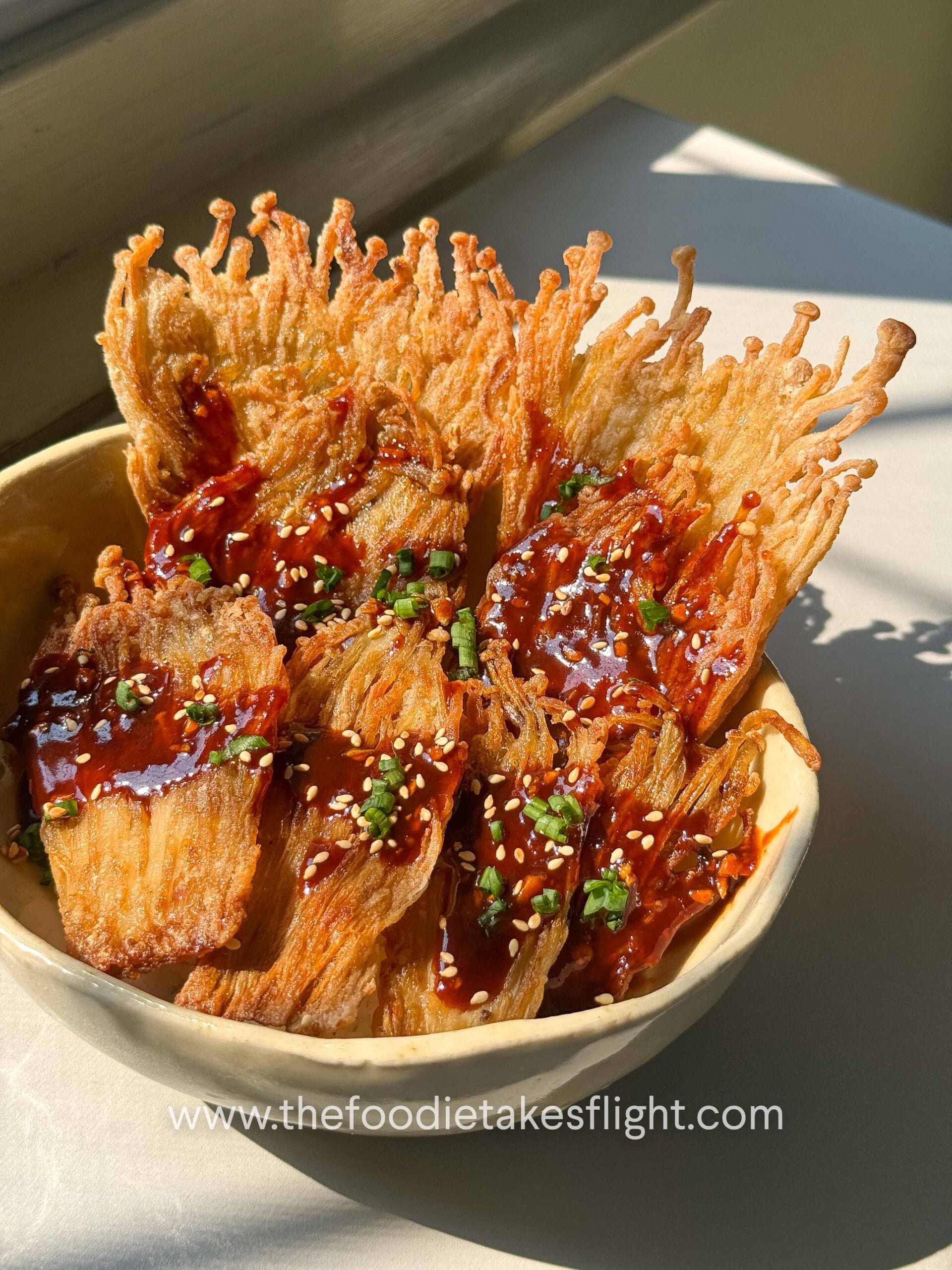 Crispy pan-fried enoki mushrooms served over rice with gochujang sauce, scallions, and sesame seeds