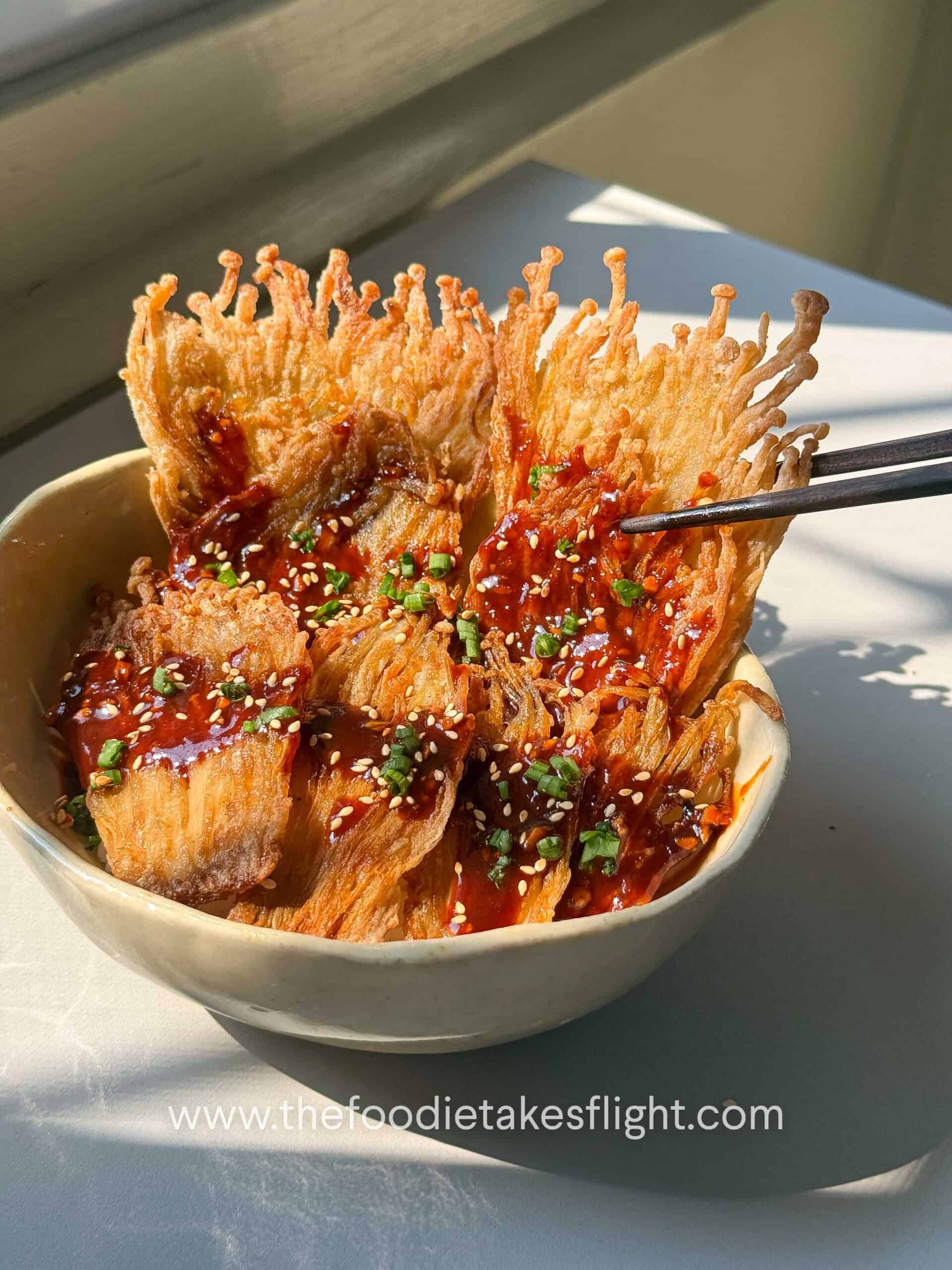 Crispy pan-fried enoki mushrooms served over rice with gochujang sauce, scallions, and sesame seeds