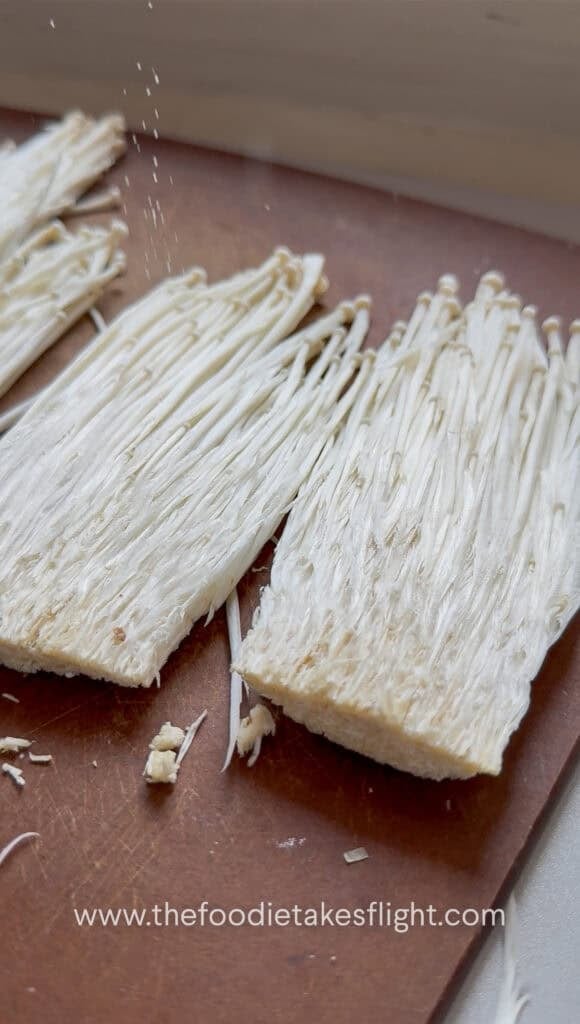 sliced enoki mushrooms on a wooden cutting board