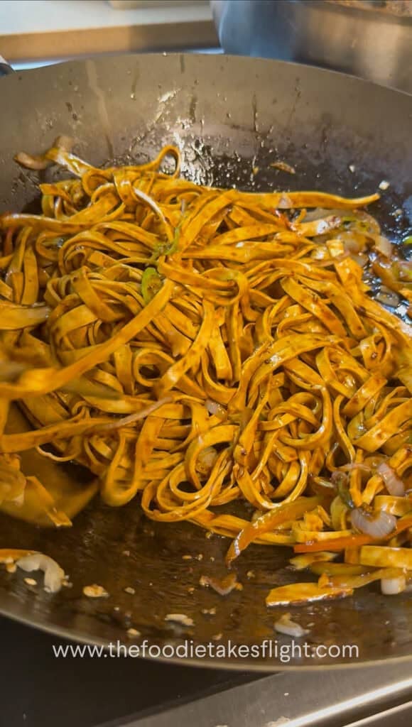 tossing the noodles to coat in the sauce