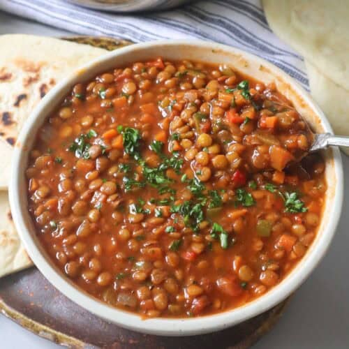 vegan lentil soup in a white bowl with a spoonful of lentils and vegetables.