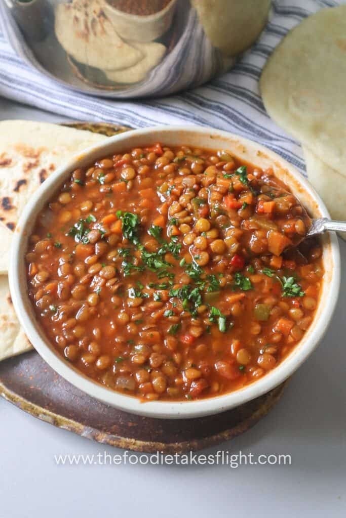 vegan lentil soup in a white bowl with a spoonful of lentils and vegetables.