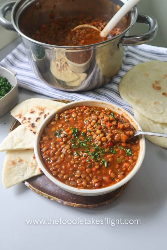 One pot lentil soup served in a white bowl with flatbread and fresh parsley.