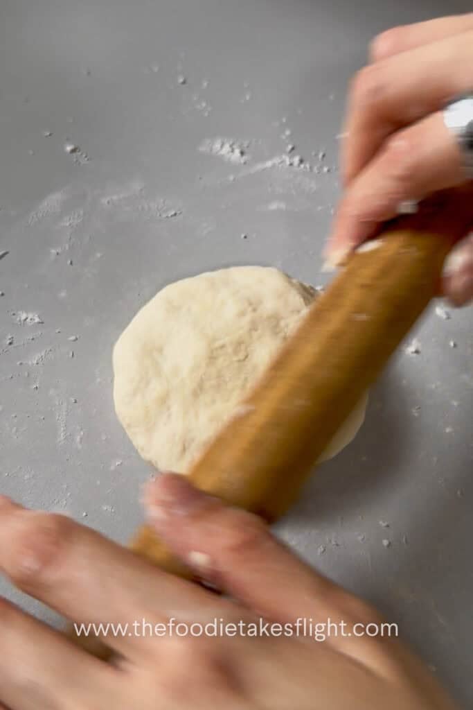 Small pita dough ball rolled into a round flatbread on a lightly floured surface