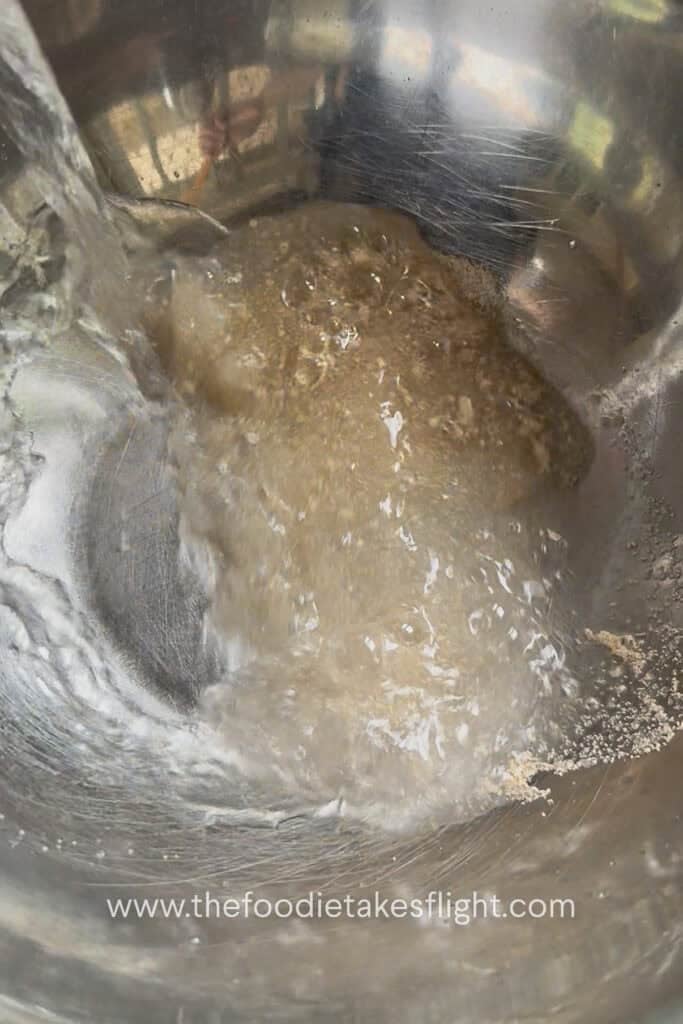 Warm water, yeast, and sugar mixed in a bowl to activate the yeast for homemade pita dough
