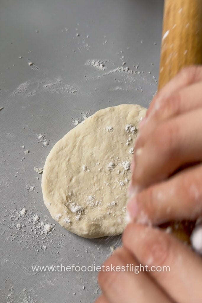 Small pita dough ball rolled into a round flatbread on a lightly floured surface