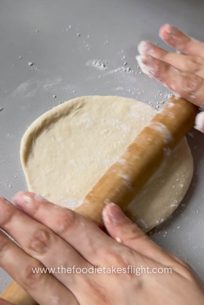 Small pita dough ball rolled into a round flatbread on a lightly floured surface