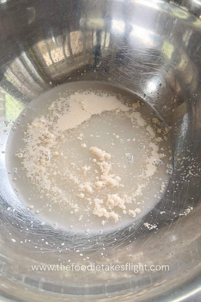 Warm water, yeast, and sugar mixed in a bowl to activate the yeast for homemade pita dough