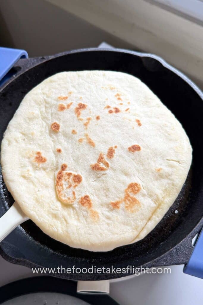 Homemade pita bread puffing on a skillet with golden brown spots