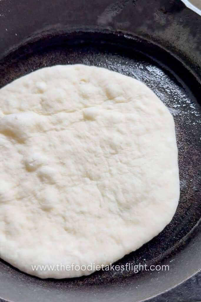 Rolled pita dough cooking on a hot skillet until bubbles form