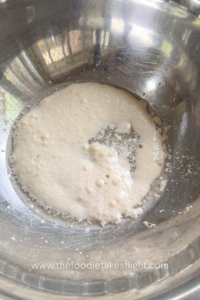 Warm water, yeast, and sugar mixed in a bowl to activate the yeast for homemade pita dough