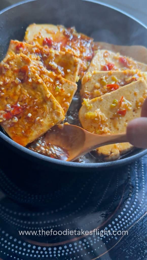 Sauce being spooned over tofu pieces as it thickens in the pan