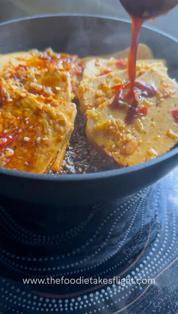 Sauce being spooned over tofu pieces as it thickens in the pan