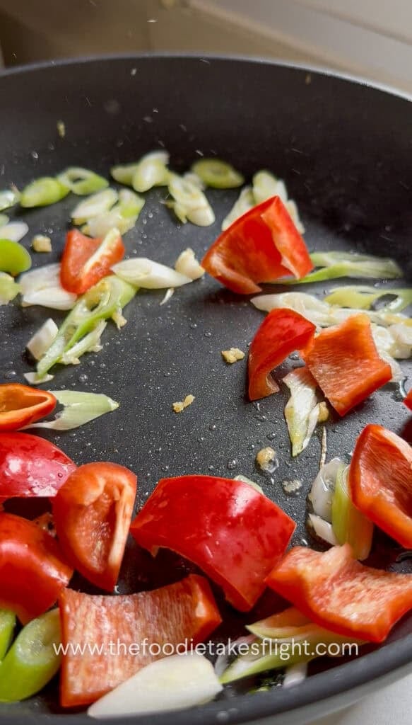 White parts of scallions, minced ginger, bell pepper stir-frying in a hot pan
