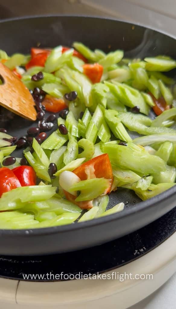 White parts of scallions, minced ginger, bell pepper, and salted black beans stir-frying in a hot pan
