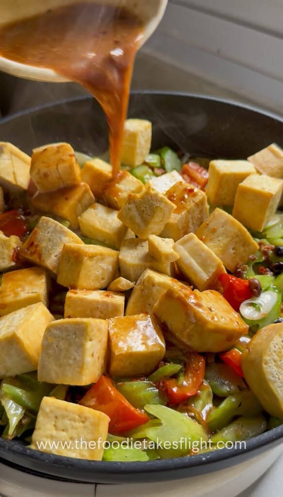Sauce poured over tofu, celery, and bell pepper in the pan