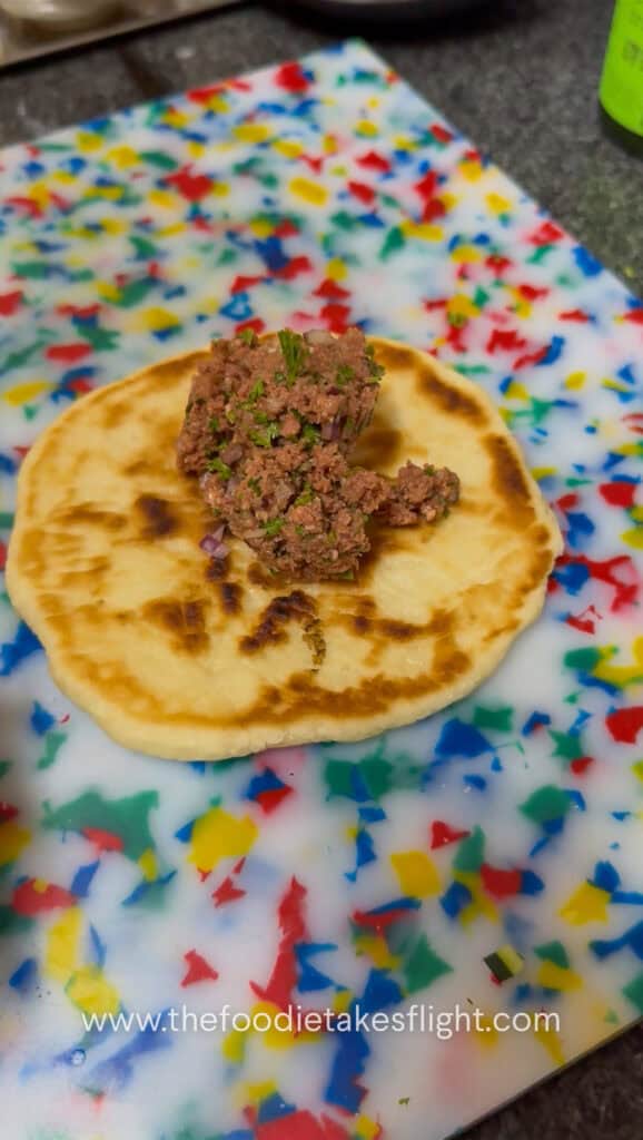 Seasoned Impossible meat spread onto the open side of pita bread before cooking