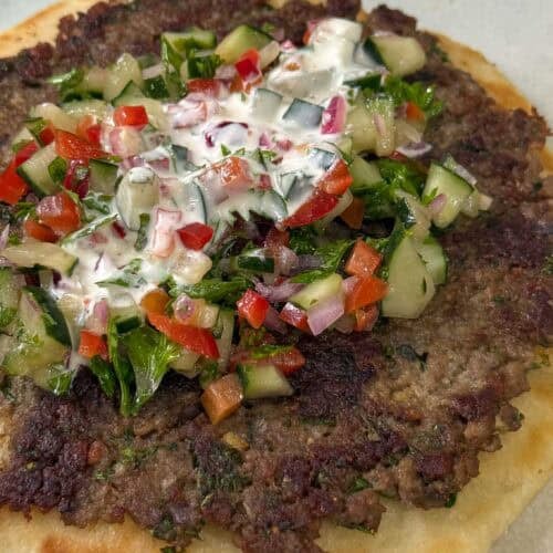 Greek-style smashed kebab pitas topped with chopped cucumber salad, parsley, and creamy yogurt dressing