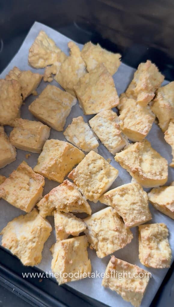 pieces of golden brown extra firm tofu broken apart in an air fryer