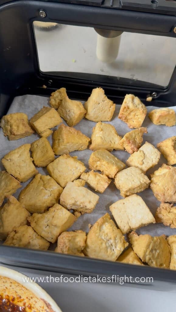 pieces of golden brown extra firm tofu broken apart in an air fryer