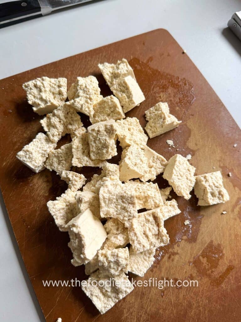 broken apart extra firm tofu on a wooden cutting board