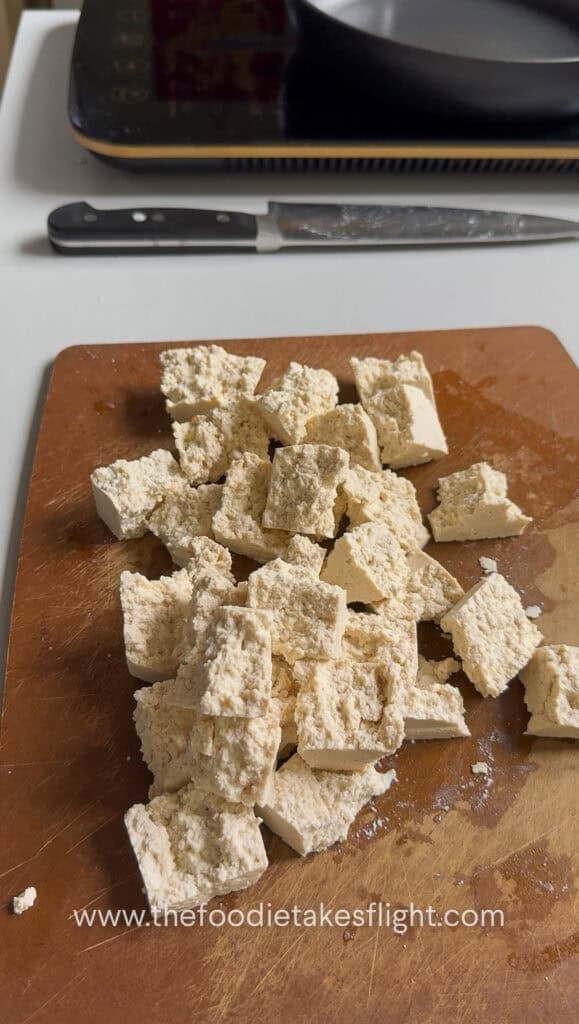 broken apart extra firm tofu on a wooden cutting board