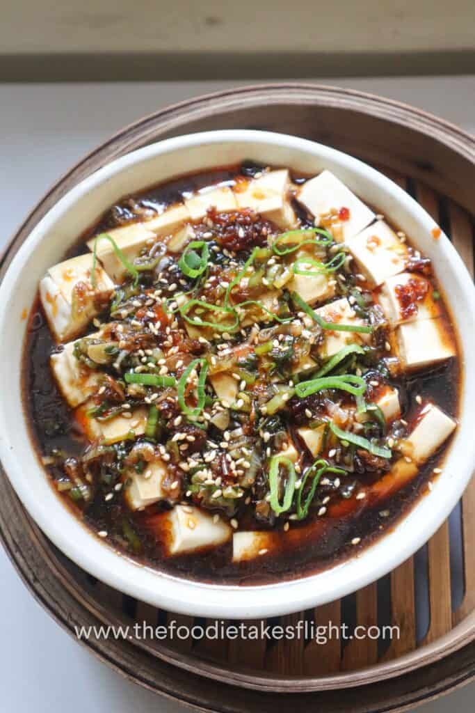 Steamed silken tofu topped with ginger scallion sauce, scallions, sesame seeds, and chili oil