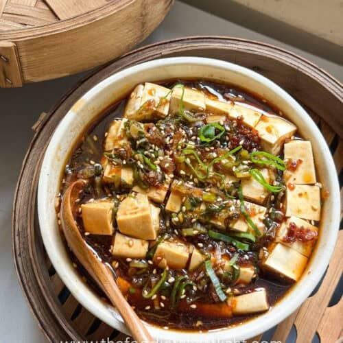 Steamed silken tofu topped with ginger scallion sauce, scallions, sesame seeds, and chili oil