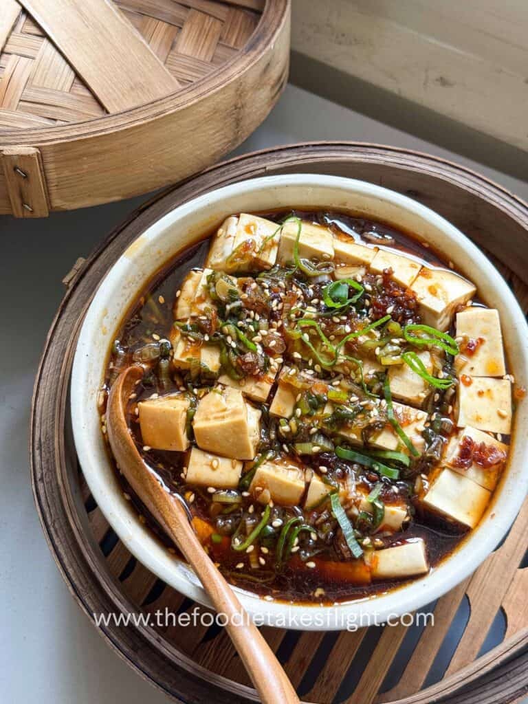 Steamed silken tofu topped with ginger scallion sauce, scallions, sesame seeds, and chili oil