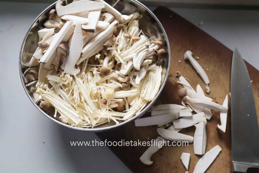 Sliced baby king oyster, shiitake, brown shimeji, and enoki mushrooms prepared for warm mushroom salad