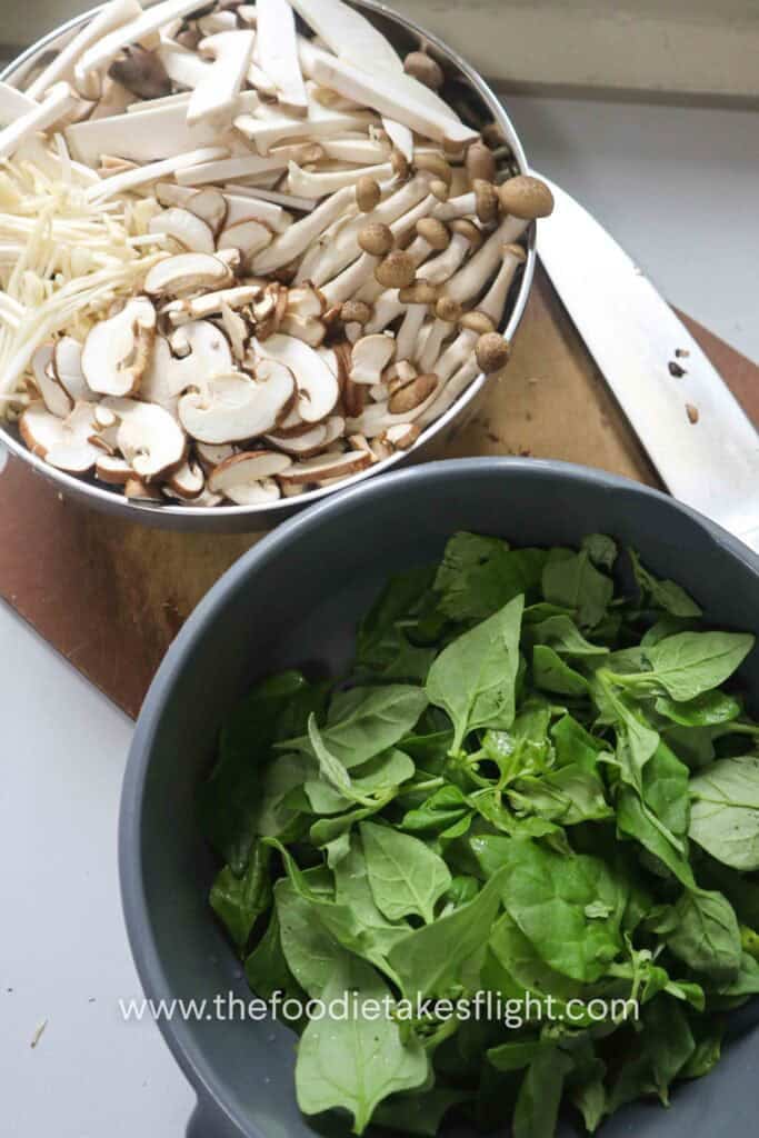 Baby king oyster, shiitake, brown shimeji, and enoki mushrooms prepared for warm mushroom salad with a bowl of fresh green spinach leaves