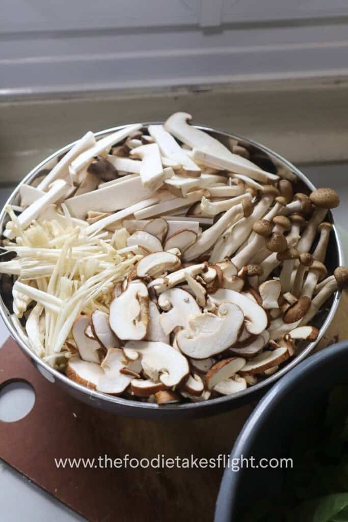 Sliced baby king oyster, shiitake, brown shimeji, and enoki mushrooms prepared for warm mushroom salad
