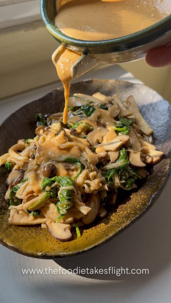 Roasted sesame dressing being poured over warm mushroom salad with spinach