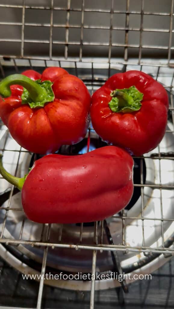 Fresh red bell peppers roasting over an open flame until charred