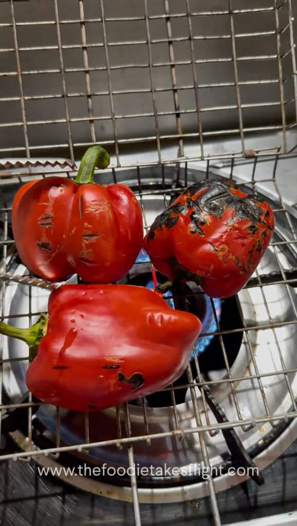 Fresh red bell peppers roasting over an open flame until charred