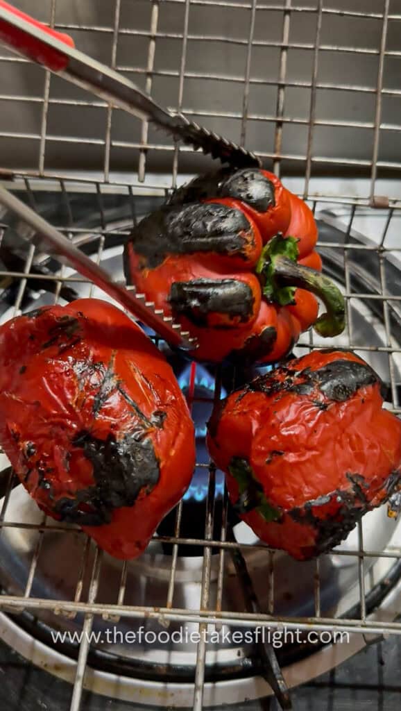 Fresh red bell peppers roasting over an open flame until charred