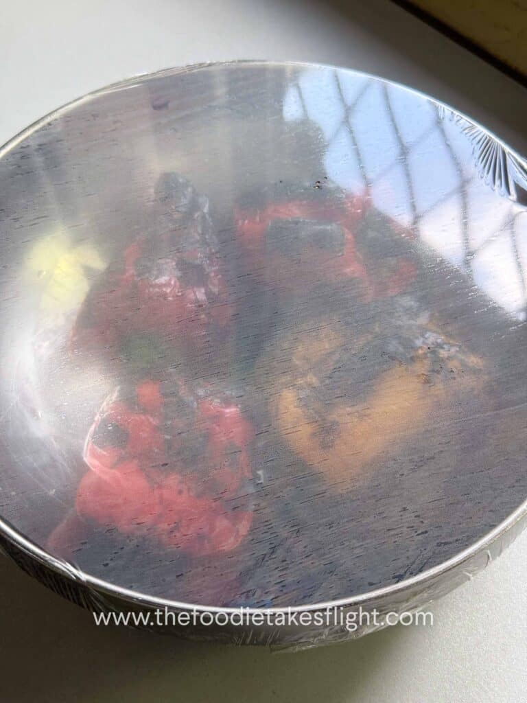 Charred red bell peppers placed in a covered bowl to steam